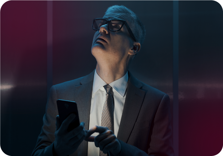Homem de terno e óculos segurando celular e olhando para cima com expressão de atenção. 