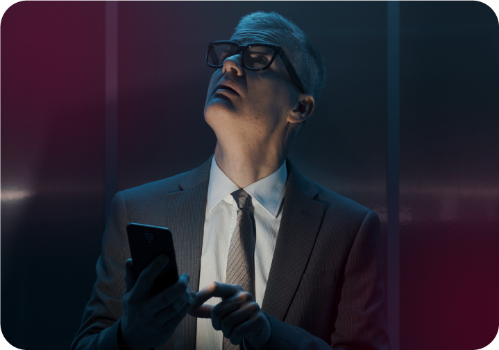 Homem de terno e óculos segurando celular e olhando para cima com expressão de atenção. 